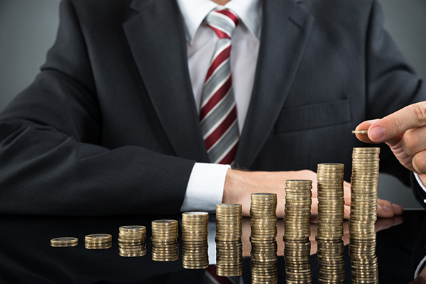 Close-up Of Businessman Placing Coin Over Stack Of Coins At Desk